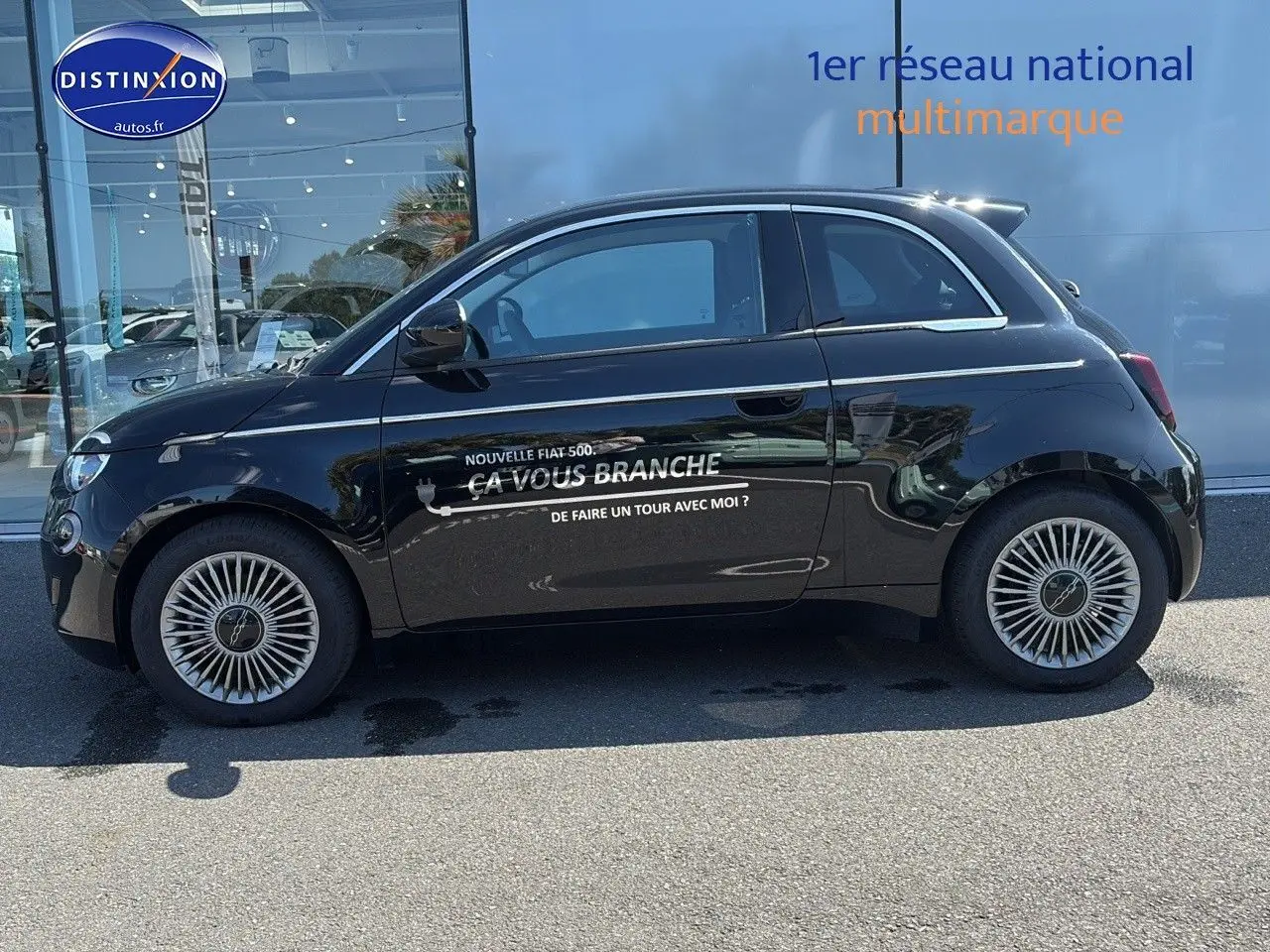 Profil côté gauche de la Fiat 500 électrique noire 2024 avec jantes alu et lettrage publicitaire sur la porte.
