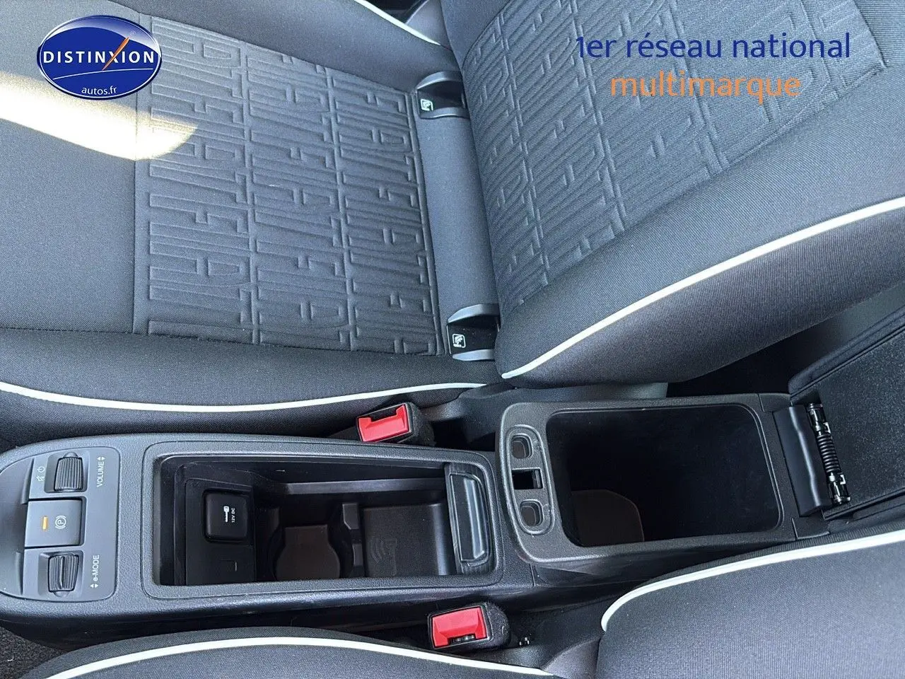 Vue plongeante sur la console centrale noire et les sièges tissu noir avec surpiqûres blanches d'une Fiat 500 électrique blanche.