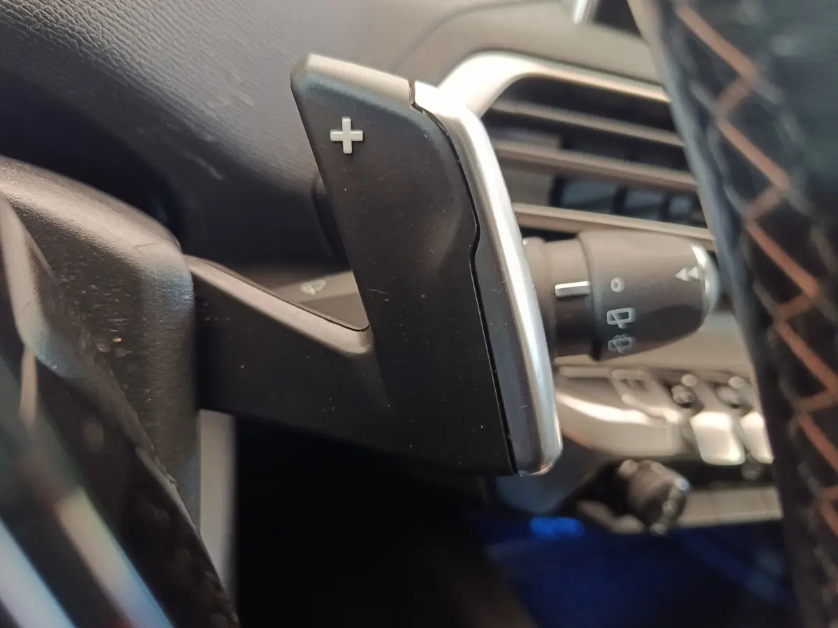 Gros plan sur la palette de changement de vitesse "+" côté droit du volant dans l'habitacle d'un Peugeot 5008 gris clair.