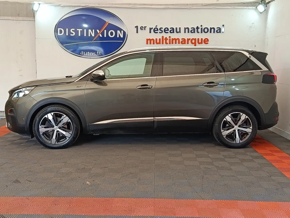 Vue de profil côté gauche d’un Peugeot 5008 GT gris clair stationné en intérieur avec jantes alliage et vitres teintées.