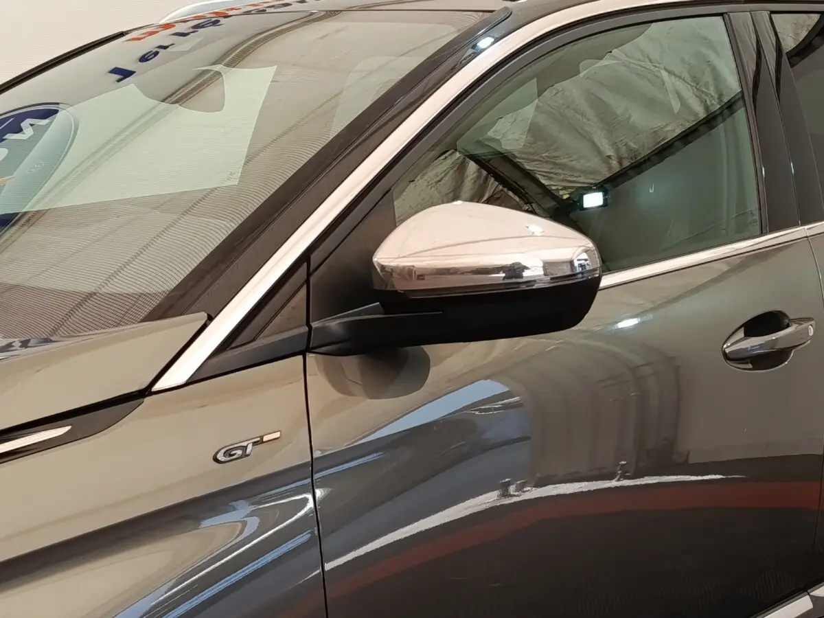 Détail du côté gauche d’un Peugeot 5008 GT gris clair avec rétroviseur chromé et badge GT visible.