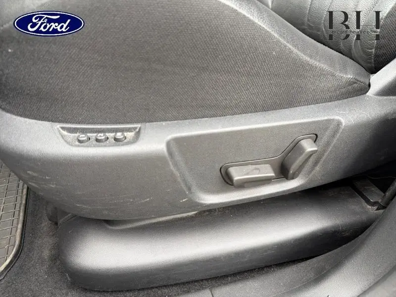 Détail des commandes de réglage électrique du siège avant en tissu gris d'un véhicule Ford, vue latérale.