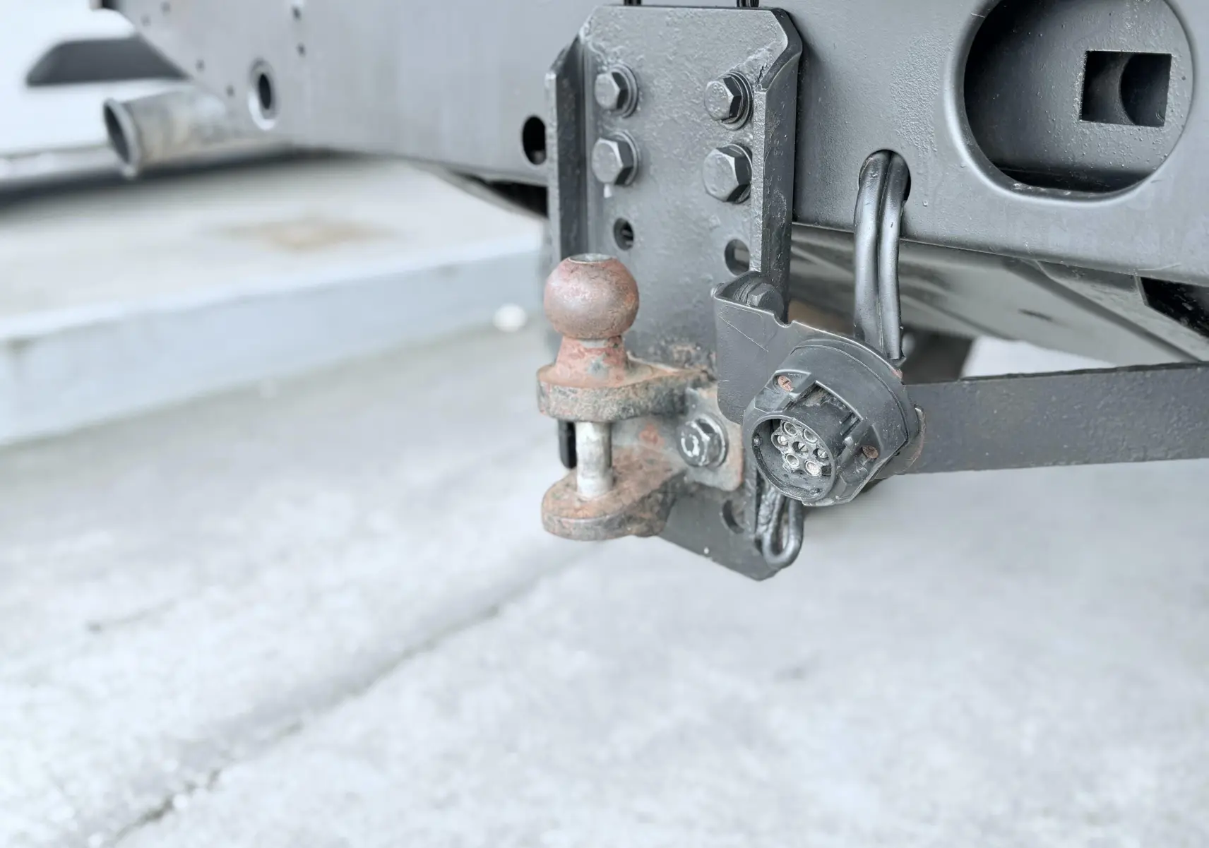 Gros plan sur l'attelage arrière rouillé et la prise électrique noire du Land Rover Defender blanc de 2007.