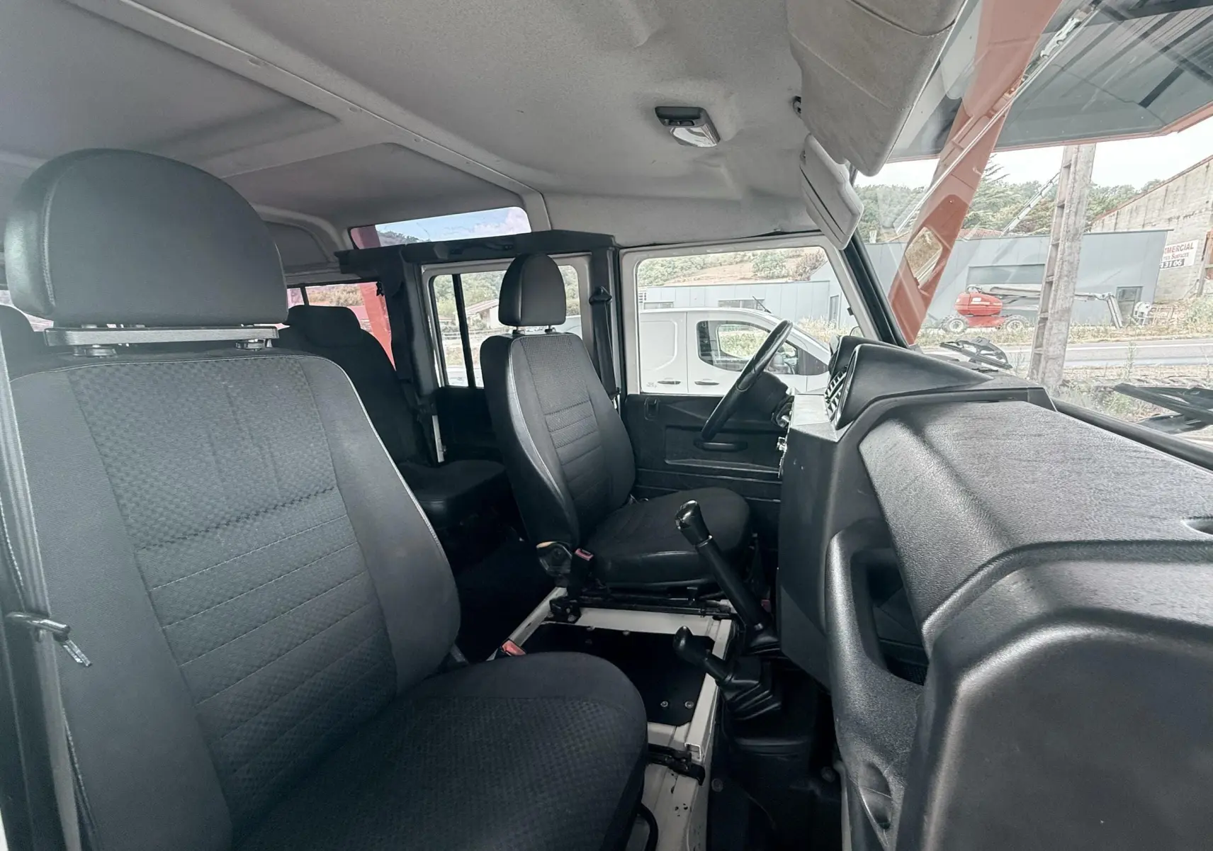 Vue intérieure côté droit du Land Rover Defender 2007, montrant les sièges tissu gris-noir et le tableau de bord noir.