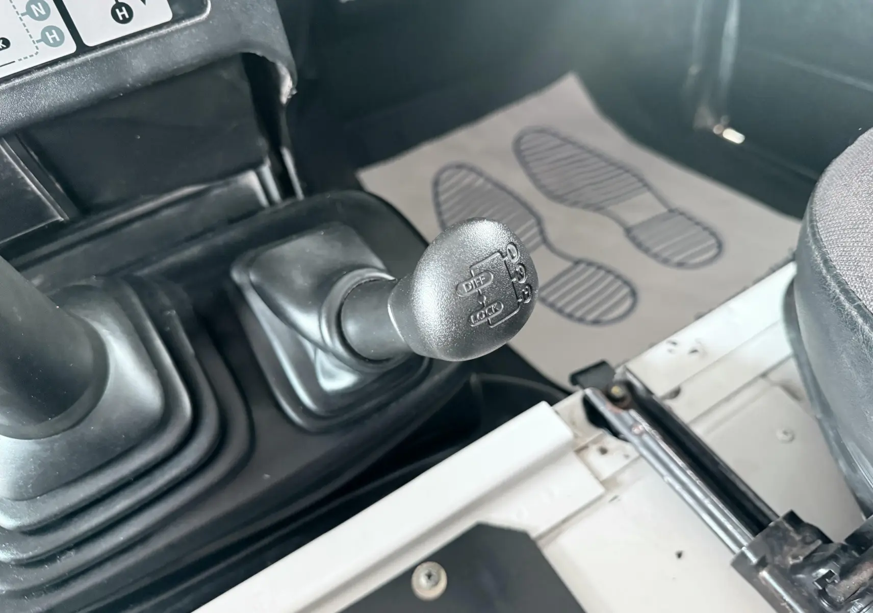 Gros plan sur le levier de vitesse manuel et la commande de différentiel du Land Rover Defender blanc de 2007, intérieur tissu gris-noir.