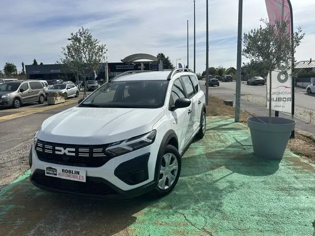 Vue 3/4 avant droite d'un Dacia Jogger blanc 2023 stationné, avec calandre noire et jantes simples.