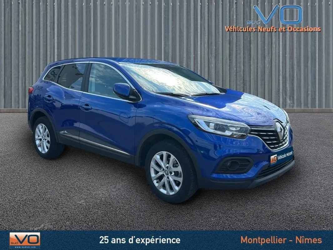 Renault Kadjar TCe 140 Business bleu foncé en 3/4 avant droit, avec jantes alliage et barres de toit visibles.