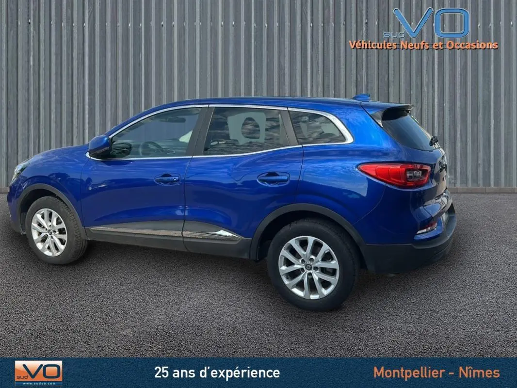 Profil latéral droit d'un Renault Kadjar TCe 140 bleu foncé avec jantes alliage et barres de toit visibles.