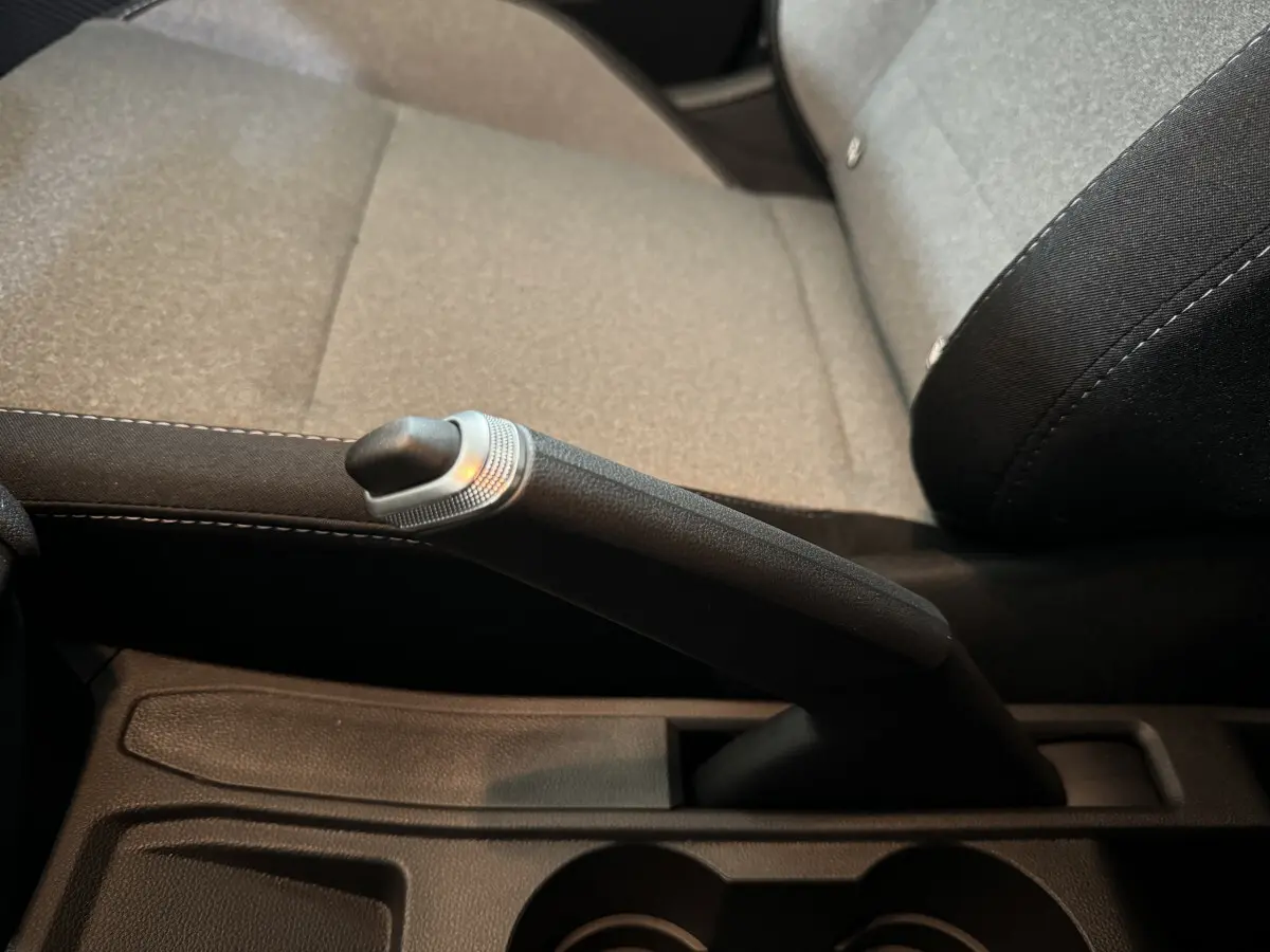 Le levier de frein à main noir en gros plan, avec la sellerie grise et noire de la Renault Clio Evolution Blue dCi 100 2025 visible en arrière-plan.