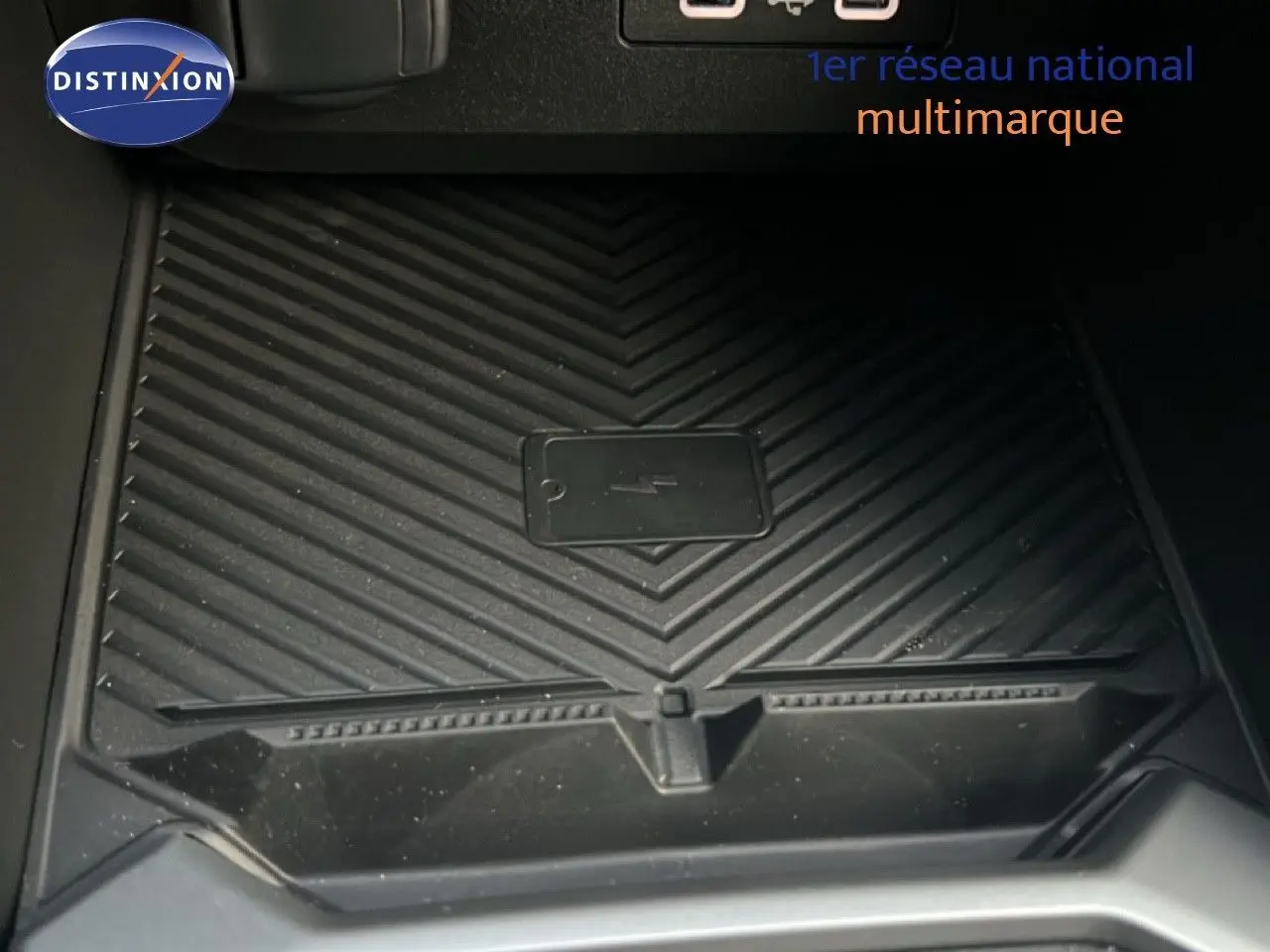 Gros plan sur le chargeur sans fil noir intégré à la console centrale du Dacia Duster blanc glacier 2025.