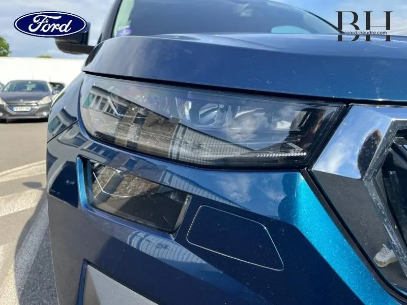 Gros plan sur le phare avant gauche bleu lave métallisé du Skoda Kodiaq 1.5 TSI 2023 avec calandre chromée.