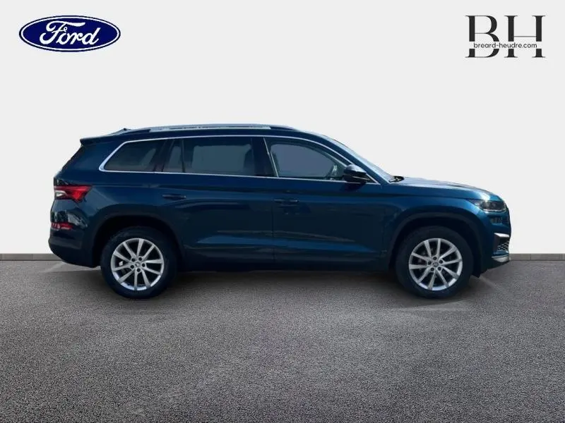 Profil droit d'un SUV SKODA KODIAQ bleu lave métallisé 2023 avec jantes alliage et barres de toit visibles.