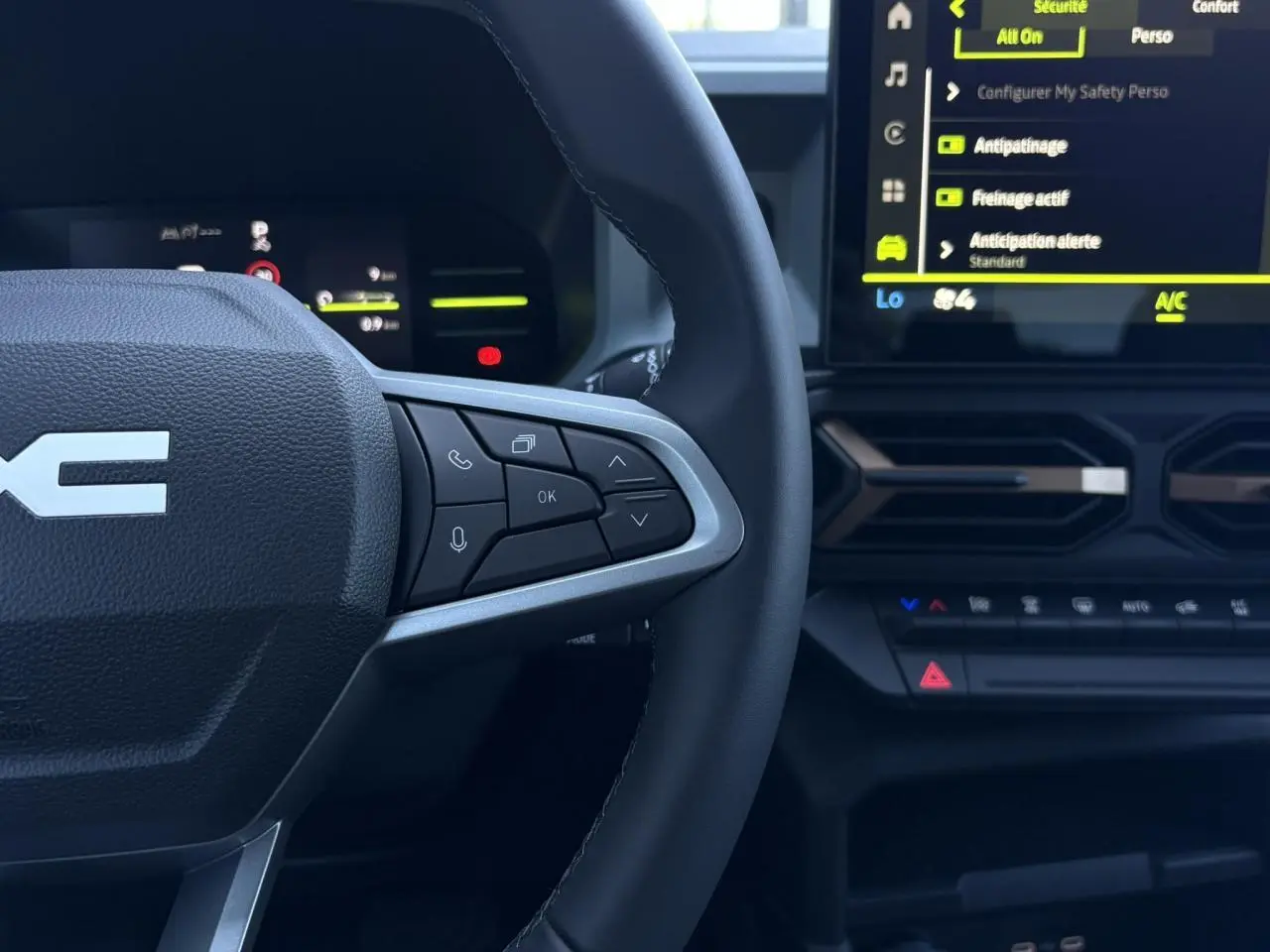Vue rapprochée du volant côté droit et écran tactile central du Dacia Duster blanc Glacier 2026, avec commandes au volant visibles.