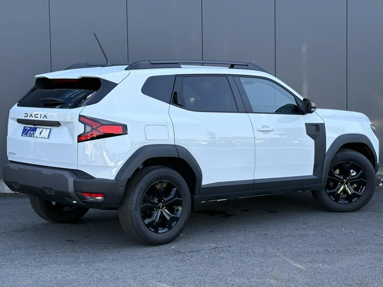Vue 3/4 arrière droite du Dacia Duster blanc Glacier avec jantes alliage noires et barres de toit noires.