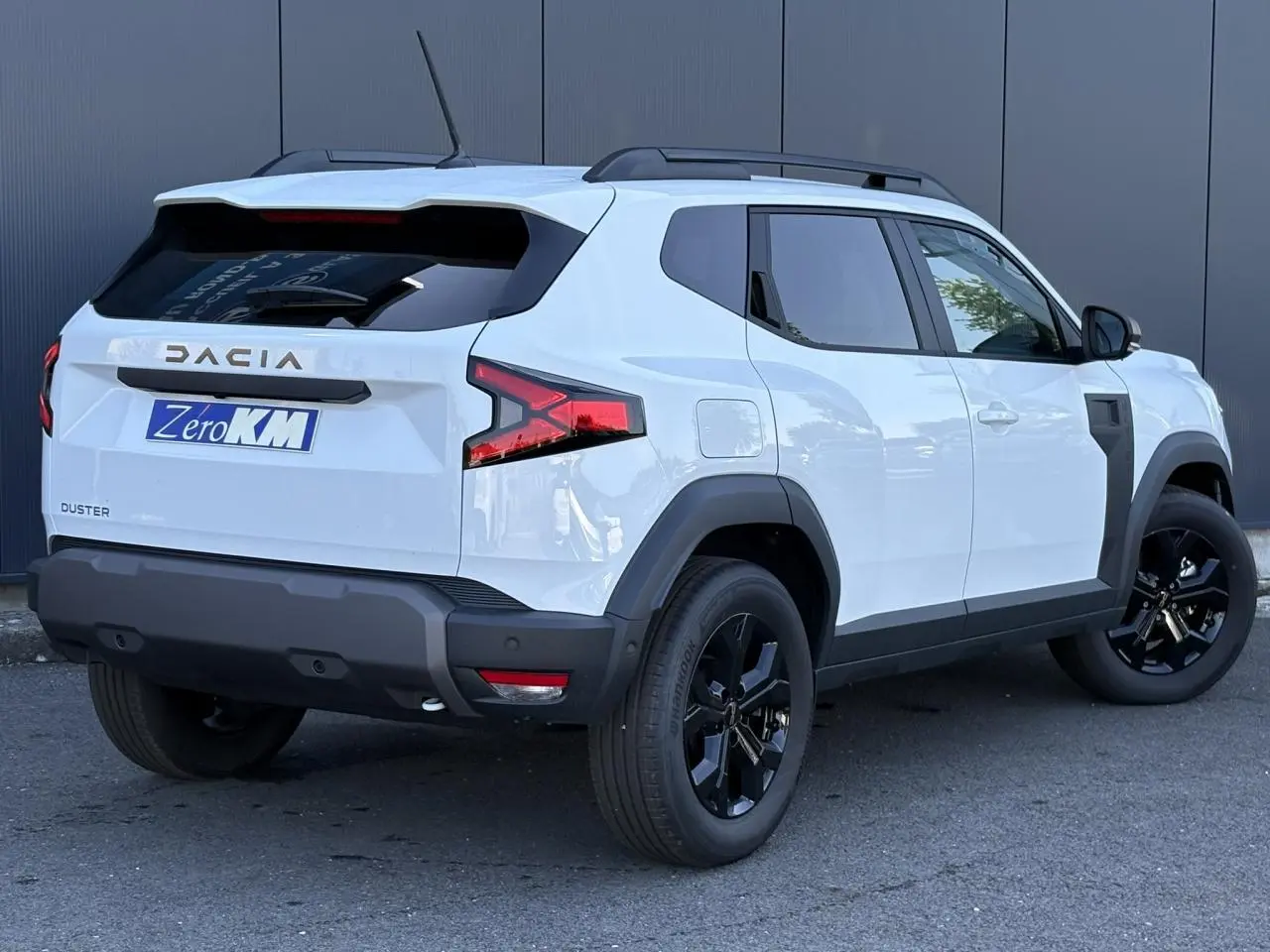 Vue 3/4 arrière droite du Dacia Duster blanc Glacier avec jantes alliage noires et barres de toit noires.