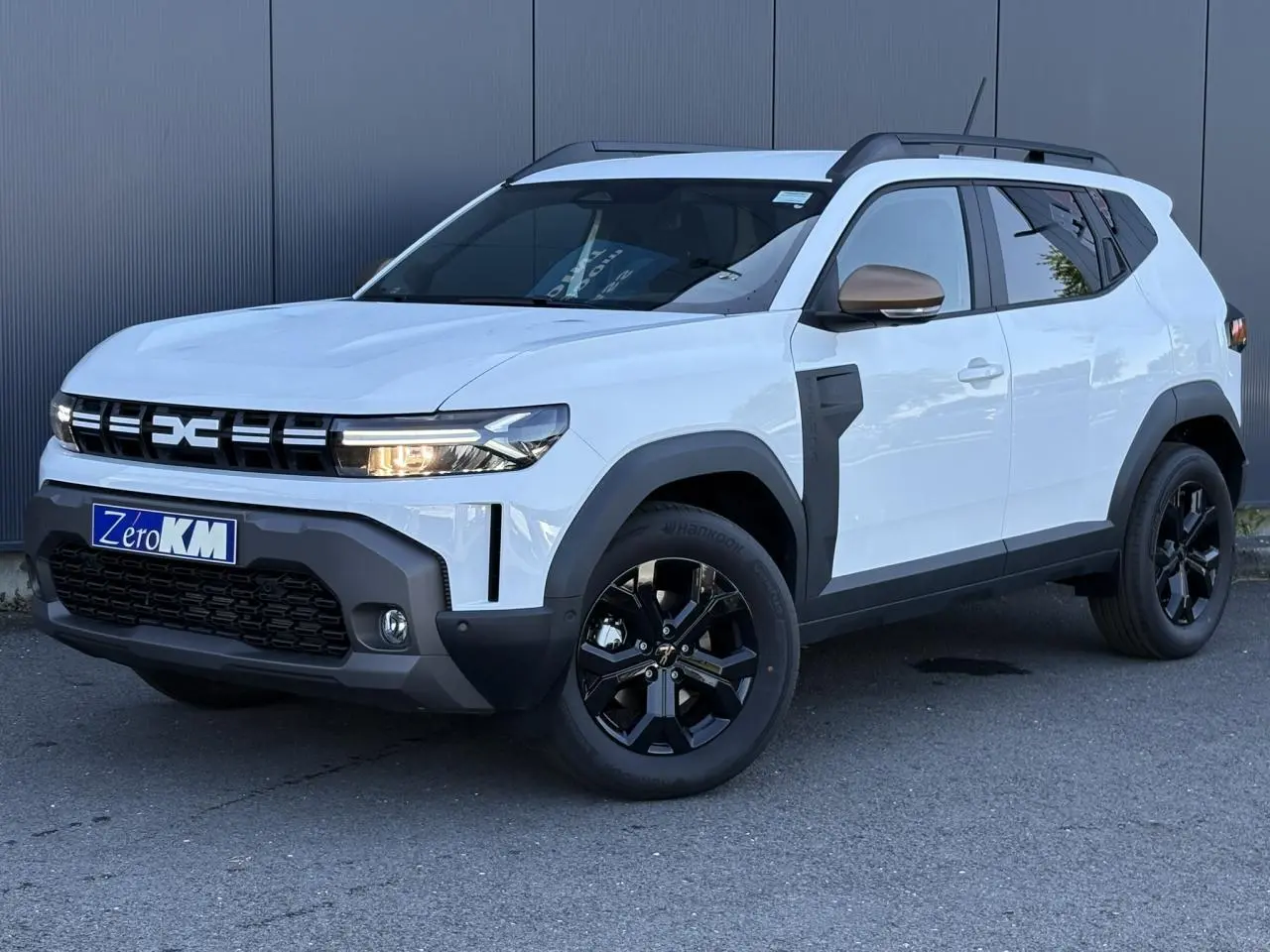 Dacia Duster ECO-G 120 Auto Extrême blanc glacier, vue 3/4 avant droit avec jantes noires et barres de toit.