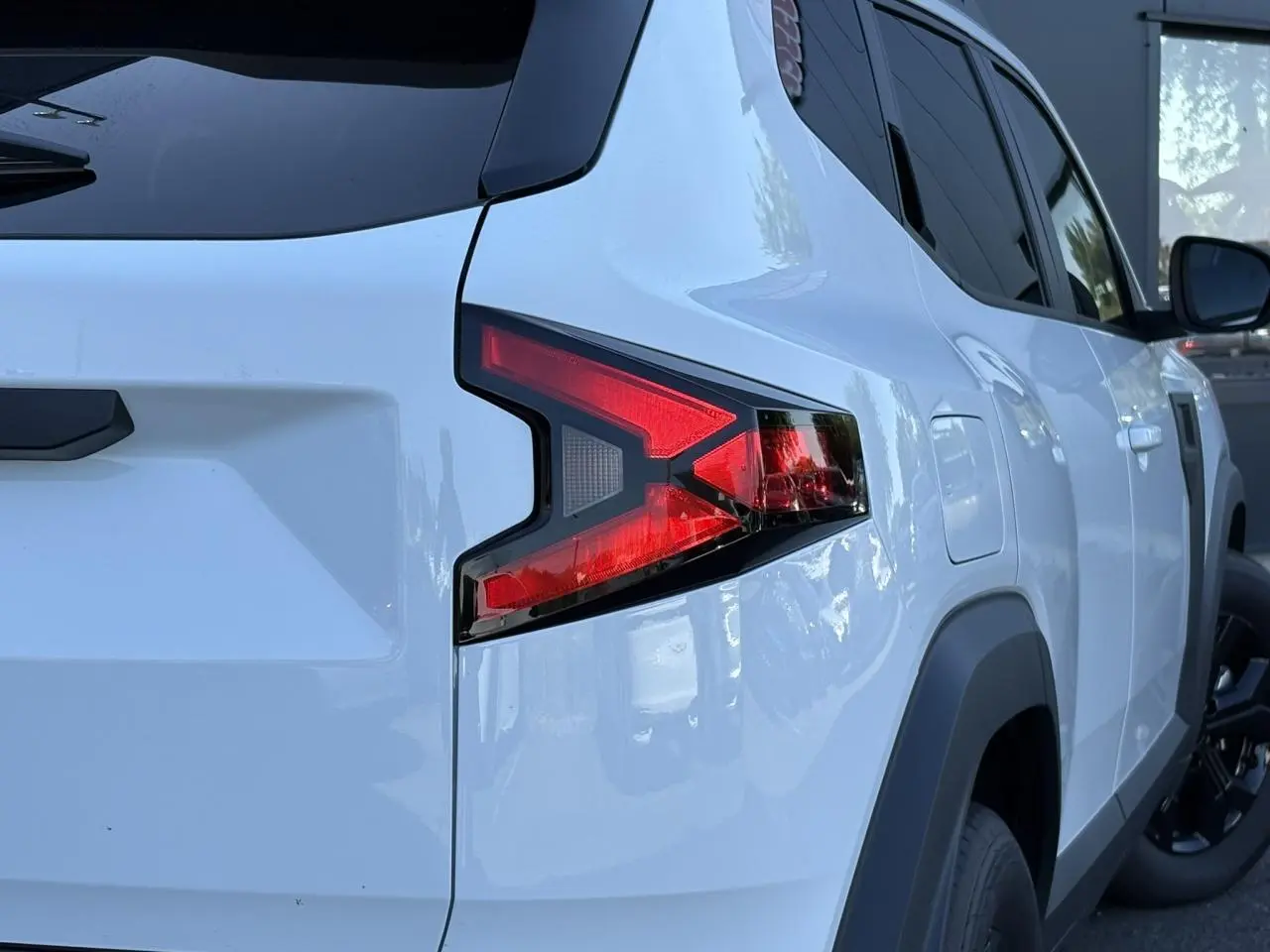 Vue arrière côté droit du Dacia Duster 2026 blanc Glacier avec feux arrière en forme de flèche et jantes noires.
