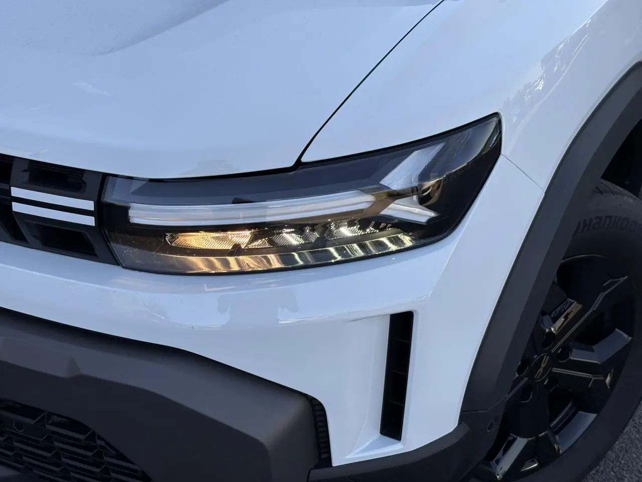 Gros plan sur l'avant droit du Dacia Duster blanc Glacier, mettant en valeur le phare LED et la jante alliage noire.