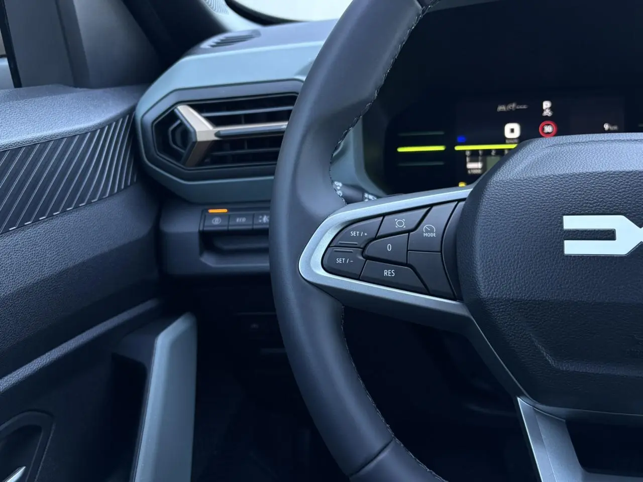 Gros plan sur le volant et la partie gauche du tableau de bord du Dacia Duster blanc Glacier, avec commandes au volant visibles.