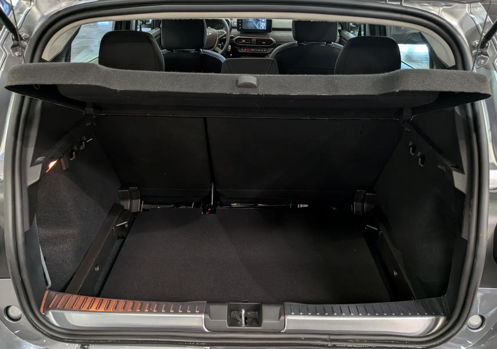 Coffre ouvert vu de l'arrière d'une Dacia Sandero Stepway 2025 gris schiste, intérieur noir et tablette arrière relevée.