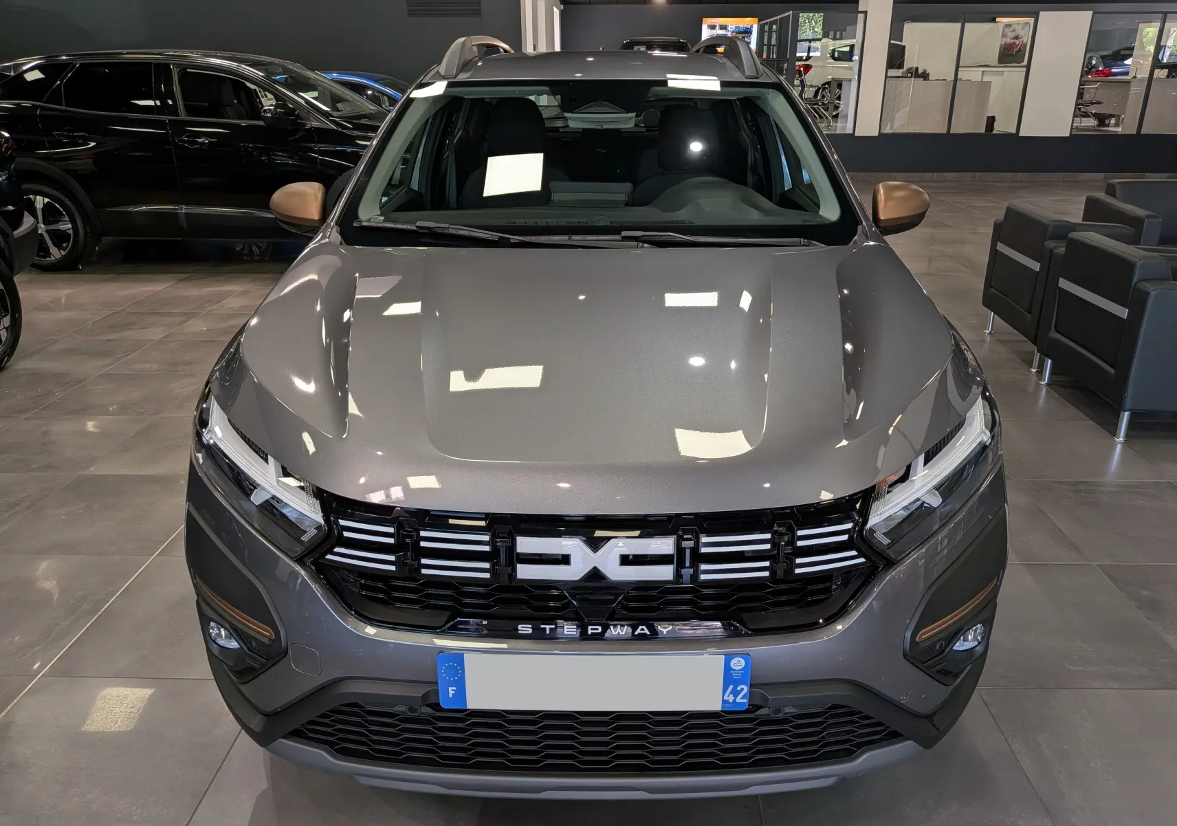 Vue avant d'une Dacia Sandero Stepway TCe 110 Gris Schiste, avec calandre noire et détails bronze sur les rétroviseurs.