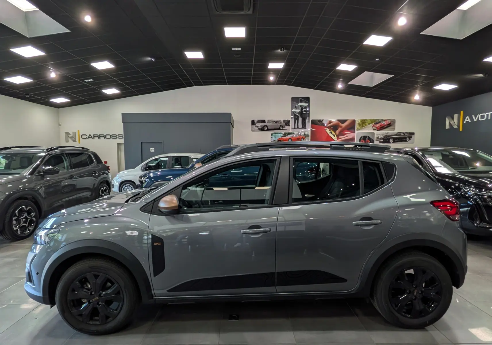 Vue de profil côté gauche d'une Dacia Sandero Stepway TCe 110 Gris Schiste avec jantes noires et coques de rétroviseurs bronze.