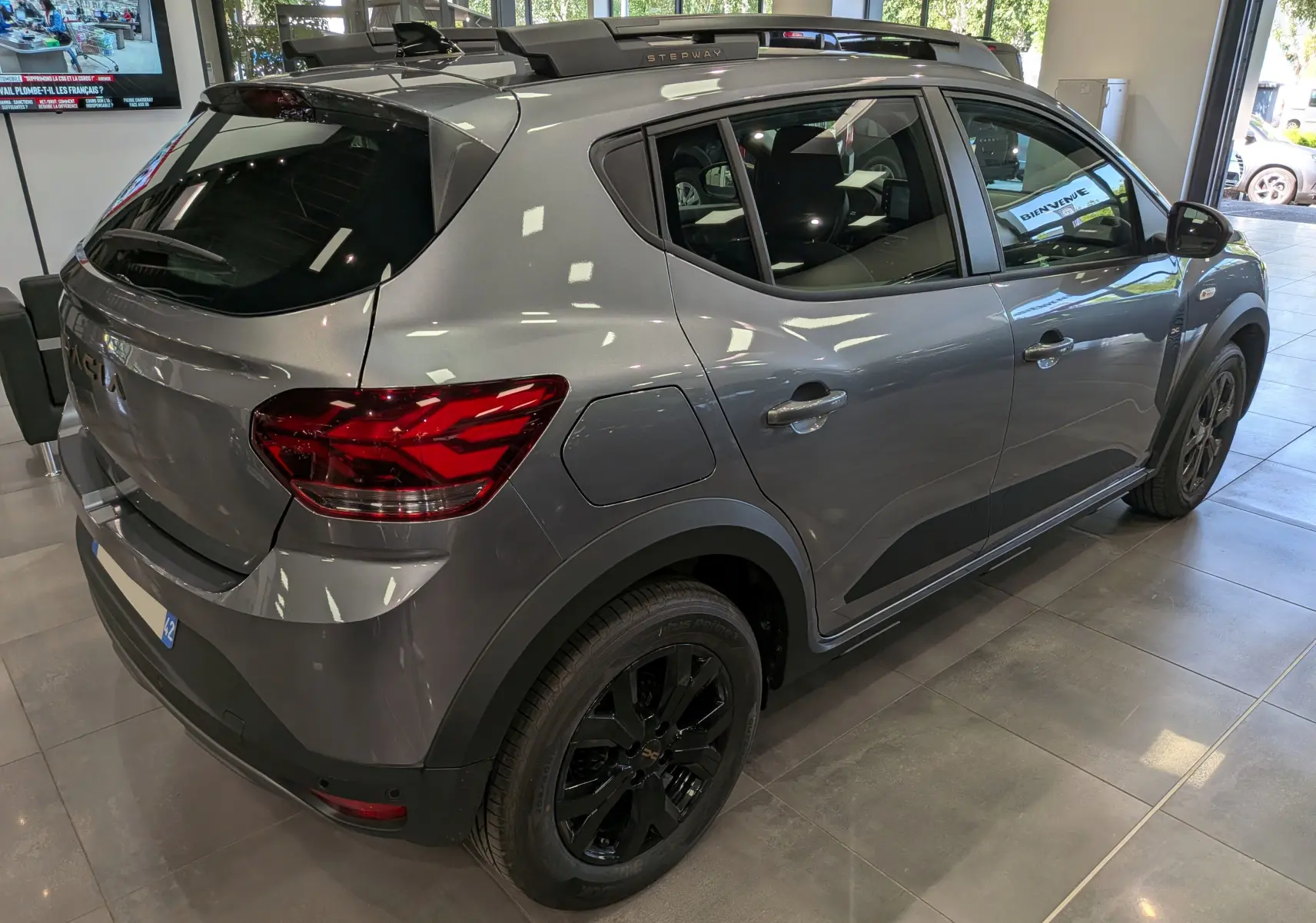 Vue 3/4 arrière droite d'une Dacia Sandero Stepway TCe 110 gris schiste avec jantes noires et toit noir en showroom.