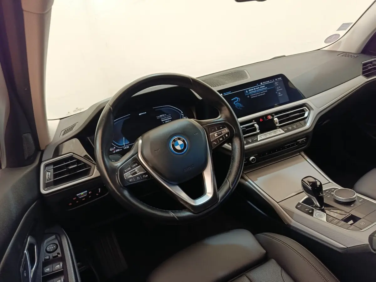 Vue intérieure côté conducteur de la BMW Série 3 320e hybride avec volant cuir, écran tactile et console centrale moderne.