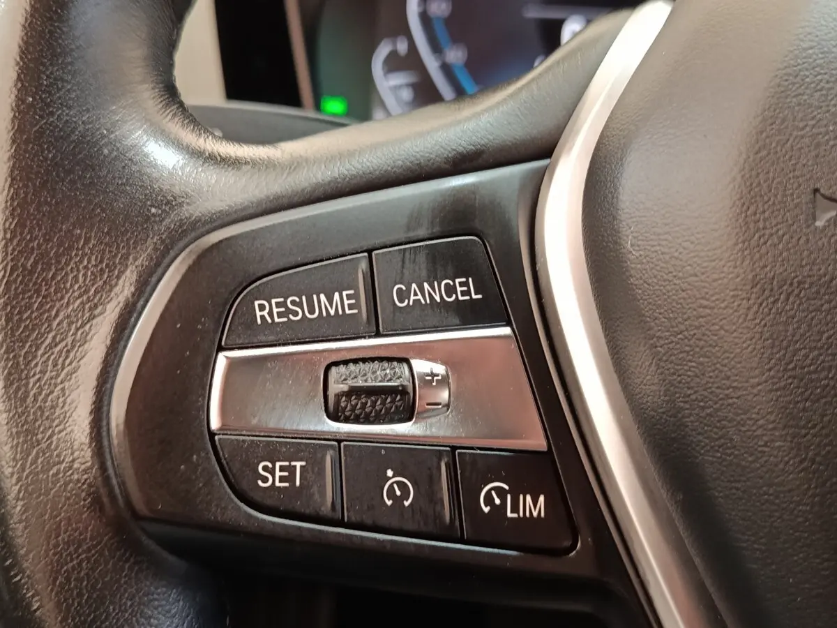 Gros plan sur les commandes de régulateur de vitesse au volant cuir noir de la BMW Série 3 320e hybride.