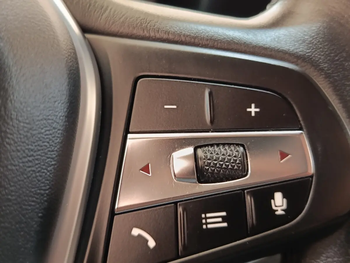 Gros plan sur les commandes multifonctions en aluminium et plastique noir du volant côté gauche d’une BMW Série 3 hybride blanche.