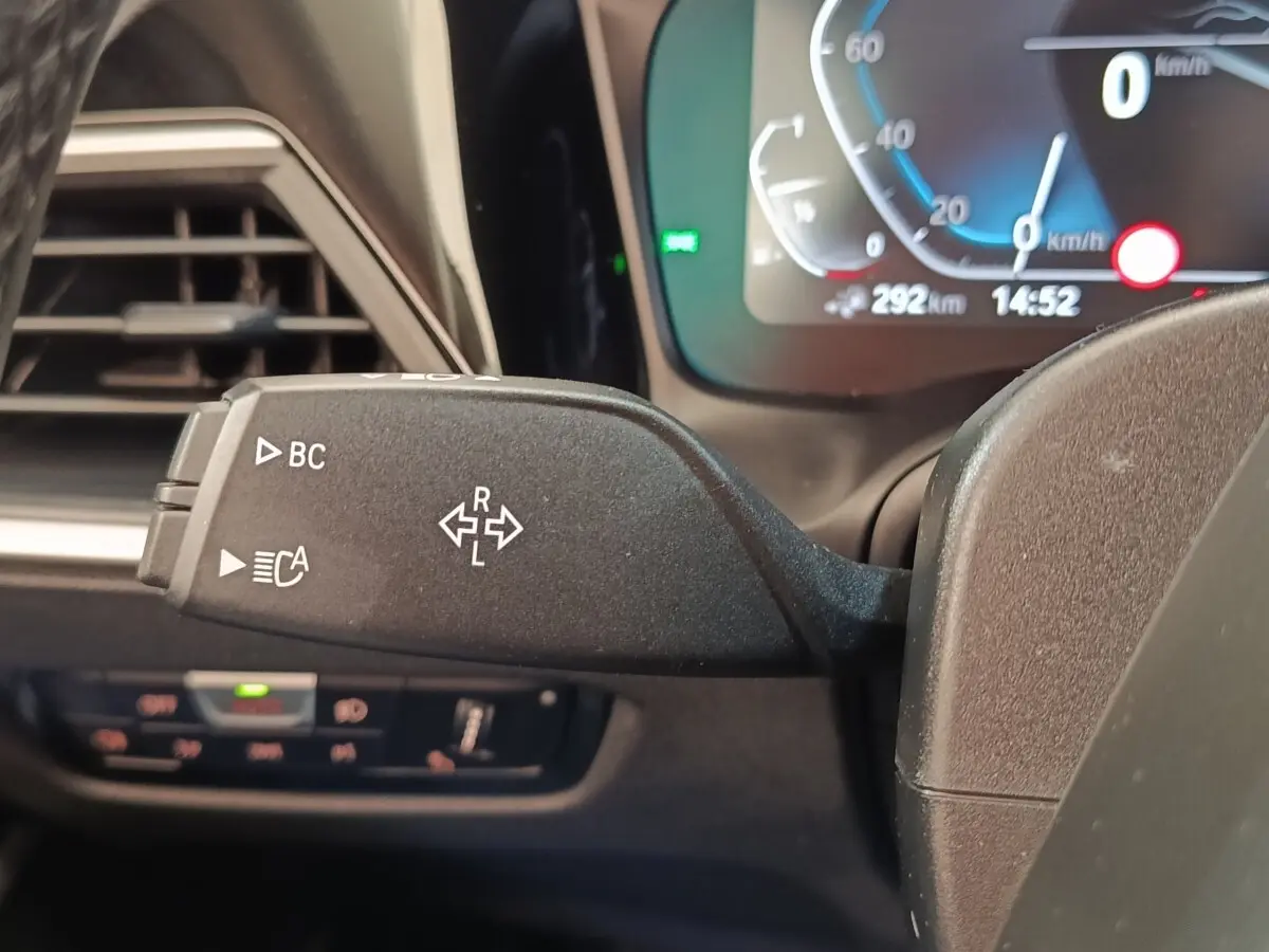 Gros plan sur la commande de clignotant gauche dans l’habitacle d’une BMW Série 3 hybride blanche, tableau de bord numérique visible.