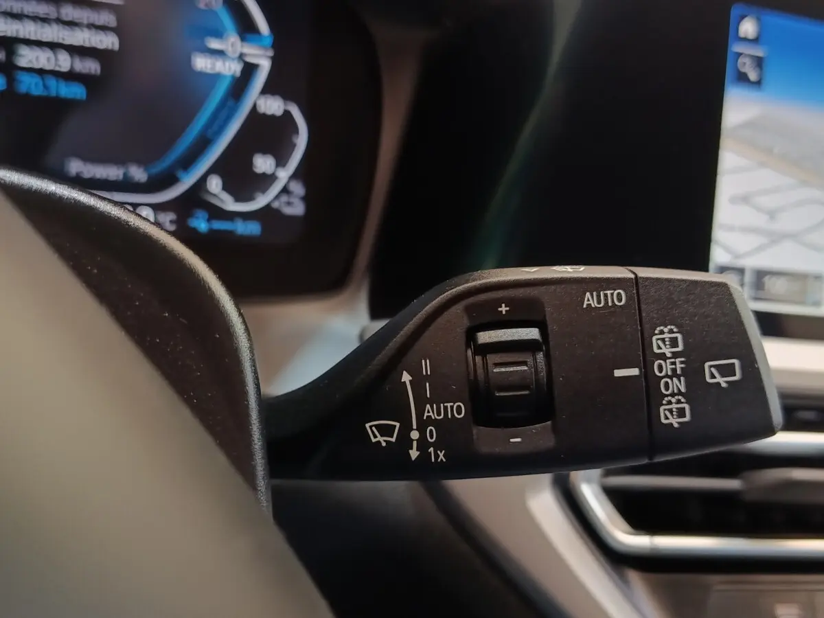Gros plan sur la commande des essuie-glaces dans l’habitacle d’une BMW Série 3 hybride blanche, avec écran tactile visible.