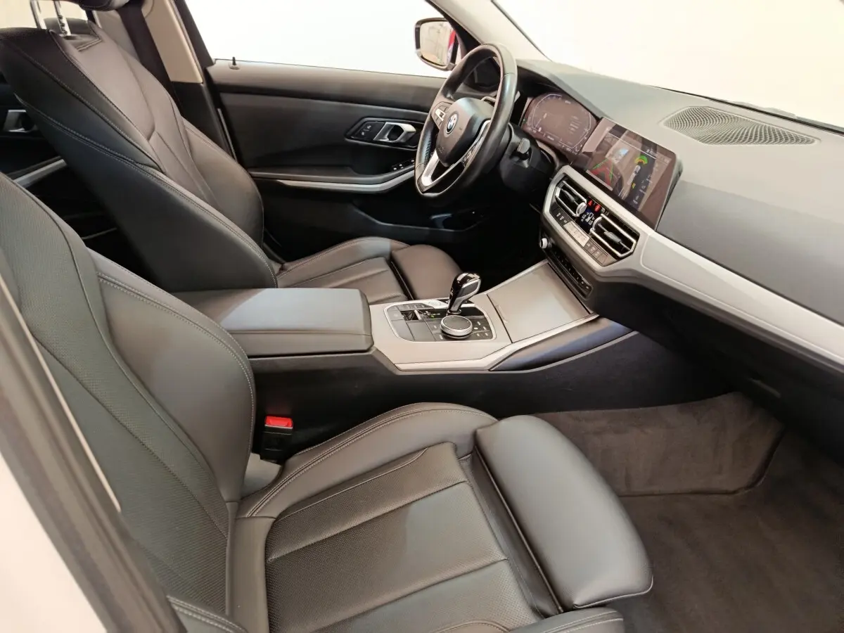 Intérieur de BMW Série 3 320e 2021 vu côté conducteur, sièges cuir noirs et tableau de bord avec écran tactile.