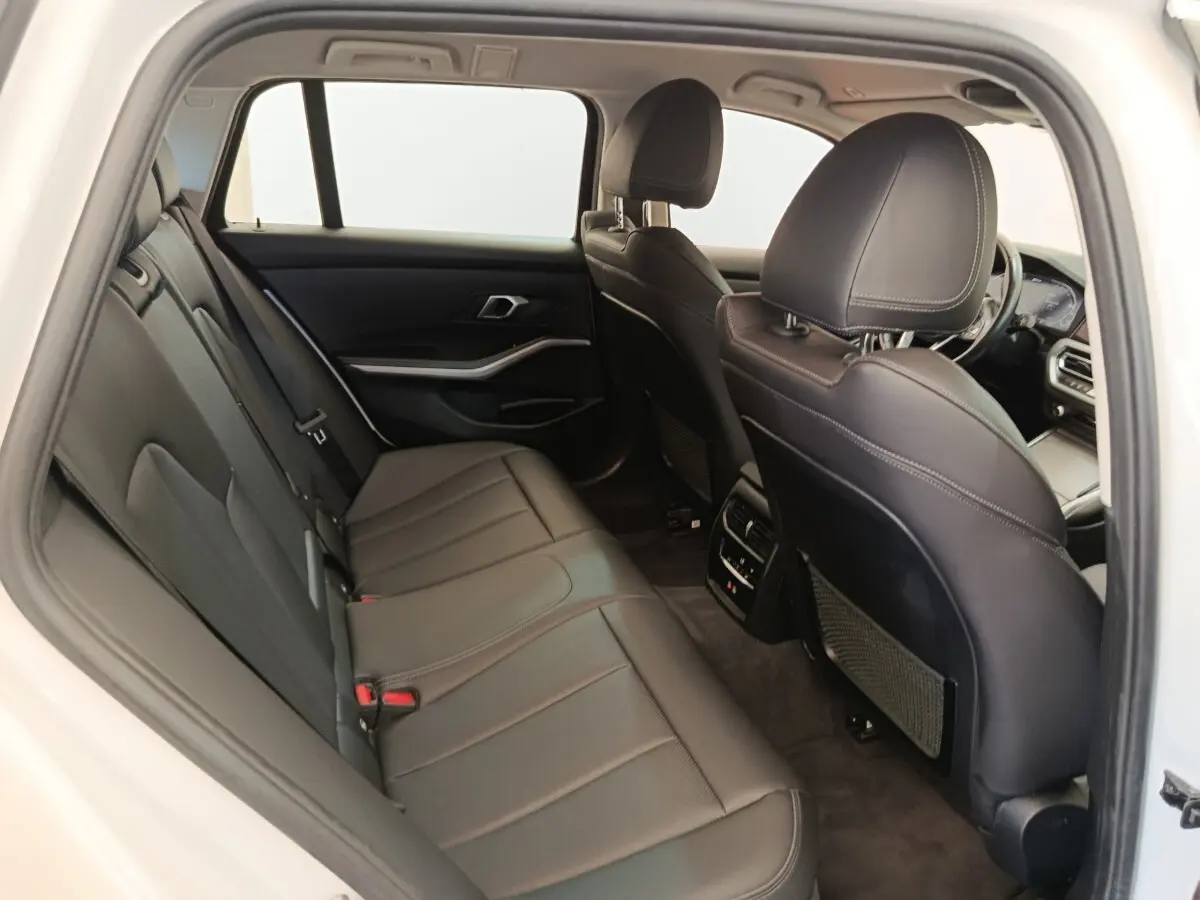 Vue intérieure arrière de la BMW Série 3 320e blanche, sièges en cuir noir et détails modernes du tableau de bord visibles.