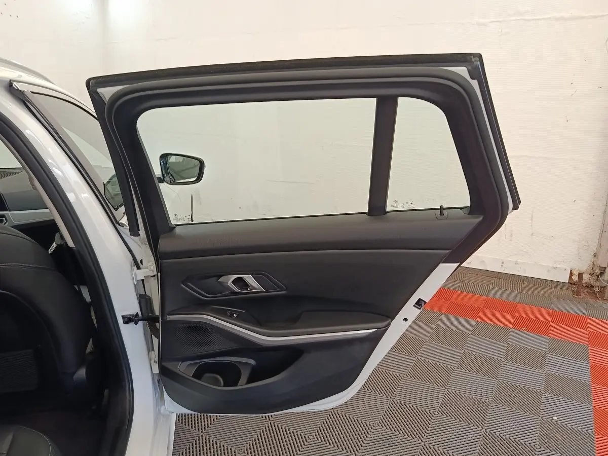 Vue intérieure de la porte arrière droite ouverte d'une BMW Série 3 320e blanche, avec garniture noire et insert alu.