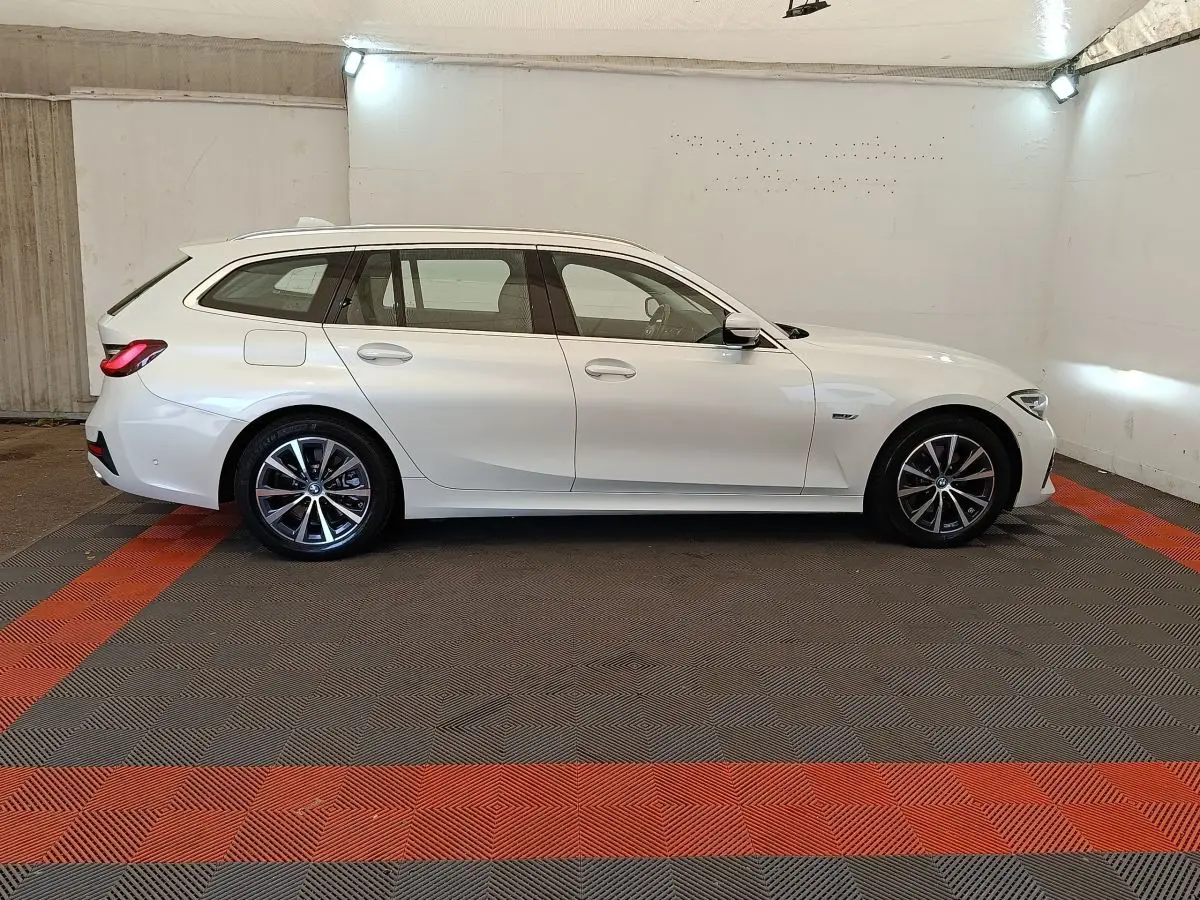 BMW Série 3 320e hybride blanche vue de profil côté gauche dans un garage avec jantes alliage noires et grises.