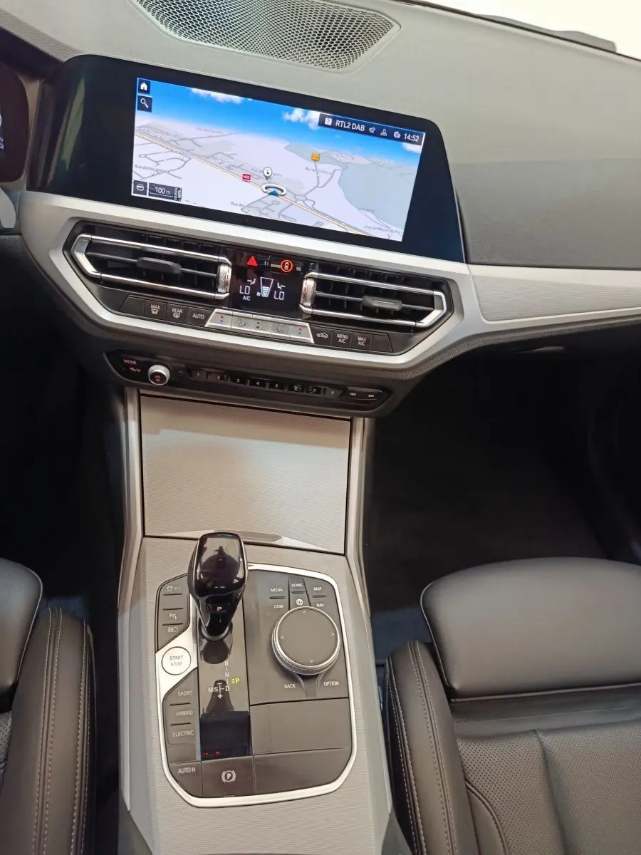 Vue intérieure centrée sur la console centrale et l’écran tactile du tableau de bord de la BMW Série 3 320e hybride.