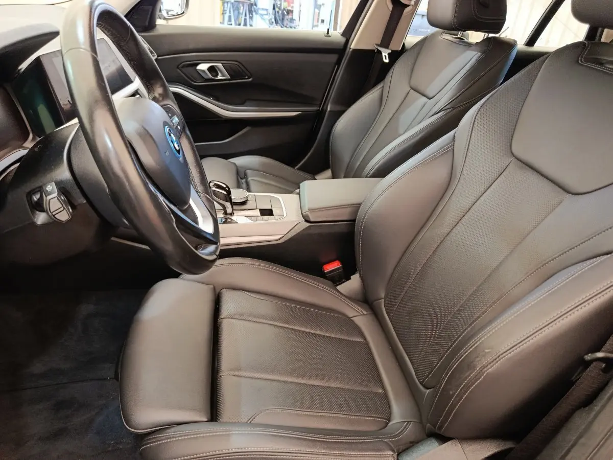 Vue intérieure côté conducteur de la BMW Série 3 320e hybride, sièges cuir noirs et volant multifonctions.