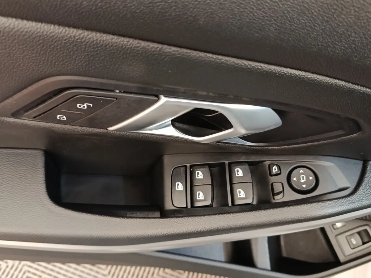 Gros plan sur la commande des vitres et la poignée intérieure noire de la porte côté conducteur d’une BMW Série 3 blanche.
