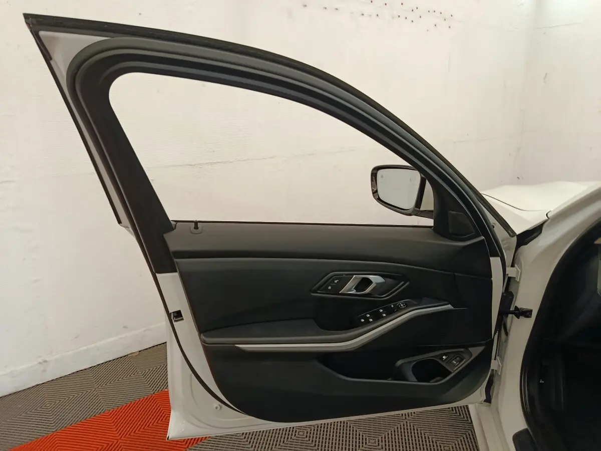Porte avant gauche ouverte d'une BMW Série 3 320e blanche, montrant le panneau intérieur noir avec commandes électriques.