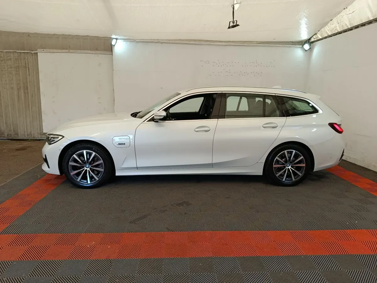 BMW Série 3 320e hybride blanche vue de profil côté gauche dans un garage avec jantes alliage et toit ouvrant.