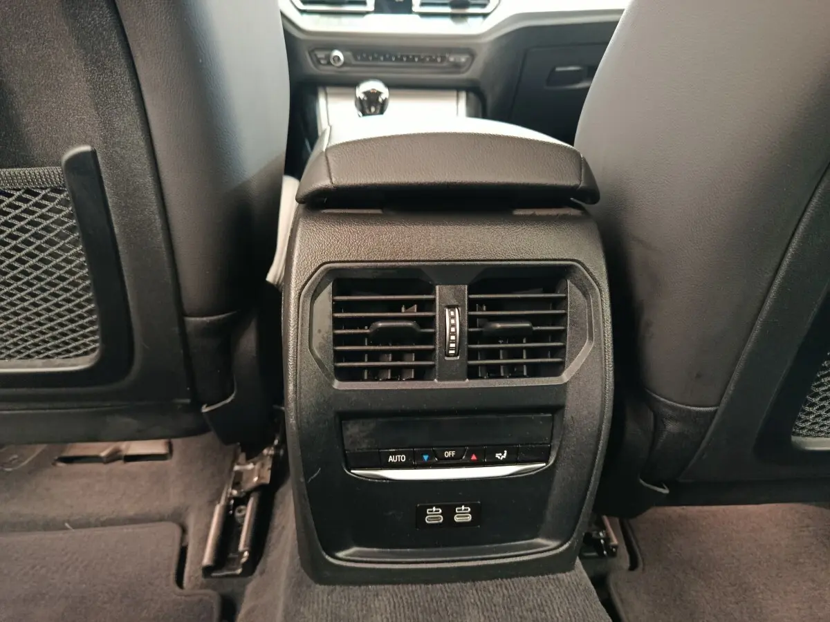 Vue rapprochée de la console centrale arrière noire avec bouches d’aération et ports USB dans BMW Série 3 blanche.