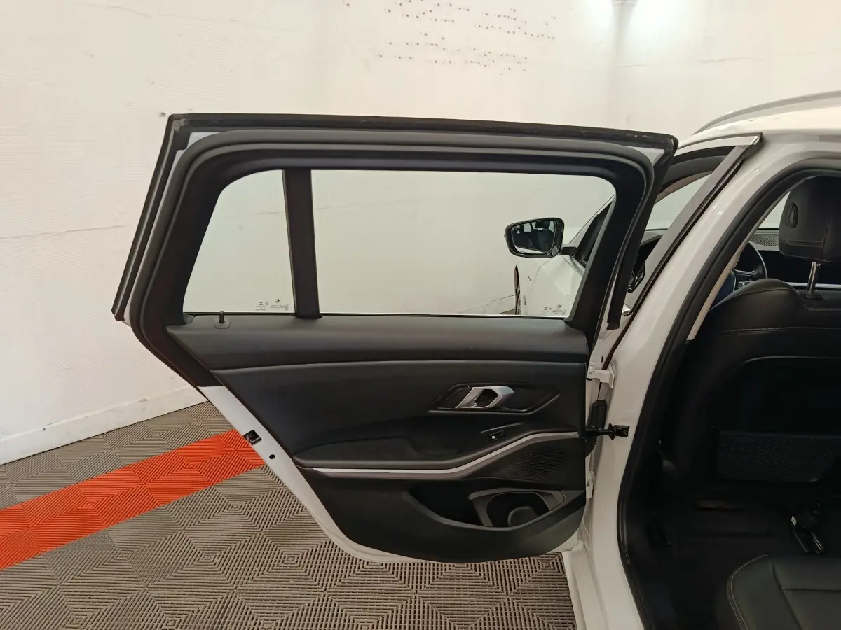 Portière arrière gauche ouverte d'une BMW Série 3 blanche, intérieur noir avec poignée métallique et haut-parleur intégré.