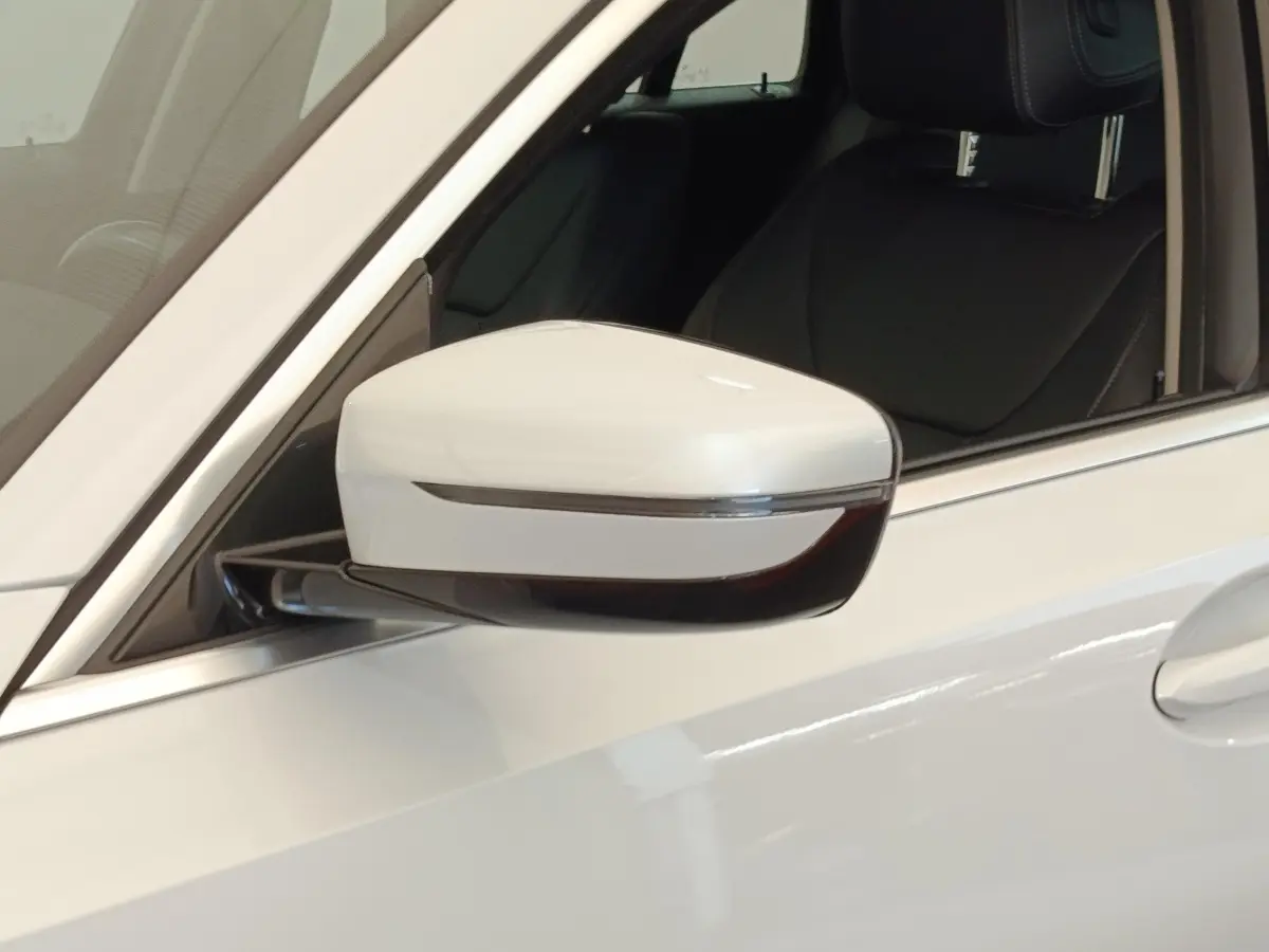 Gros plan sur le rétroviseur côté gauche blanc d’une BMW Série 3 320e hybride avec intérieur cuir noir visible.