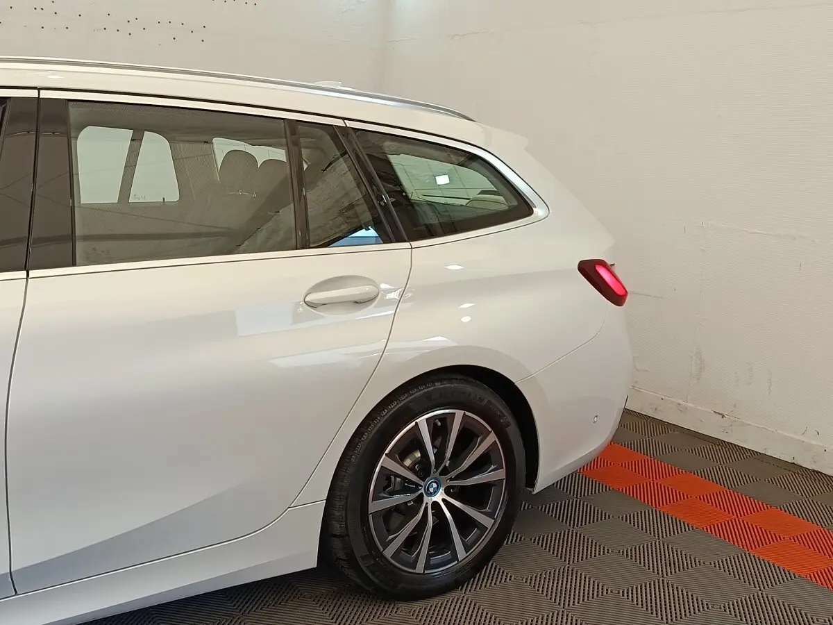 Vue arrière côté droit d’un break BMW Série 3 320e hybride blanc avec jante alliage et feux arrière allumés.
