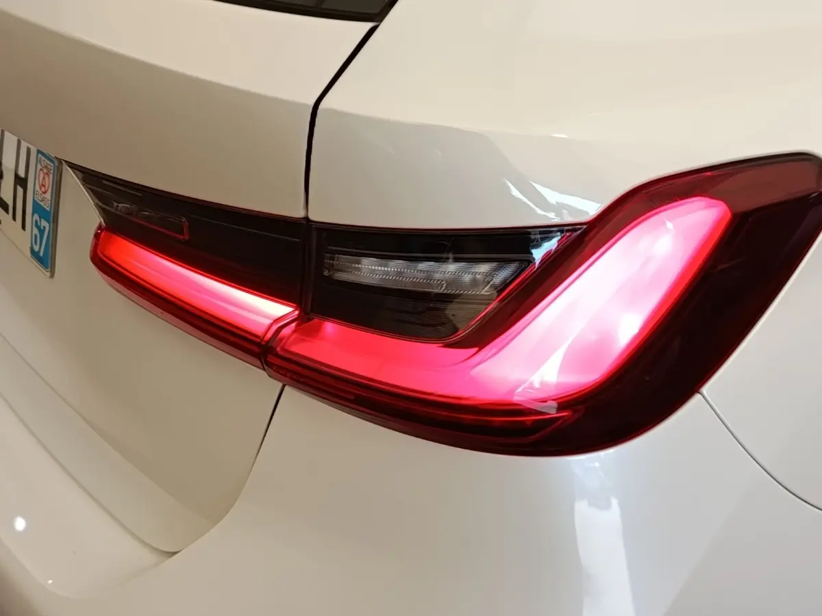 Feu arrière droit allumé d’une BMW Série 3 320e blanche, vue rapprochée du coffre et plaque d’immatriculation.