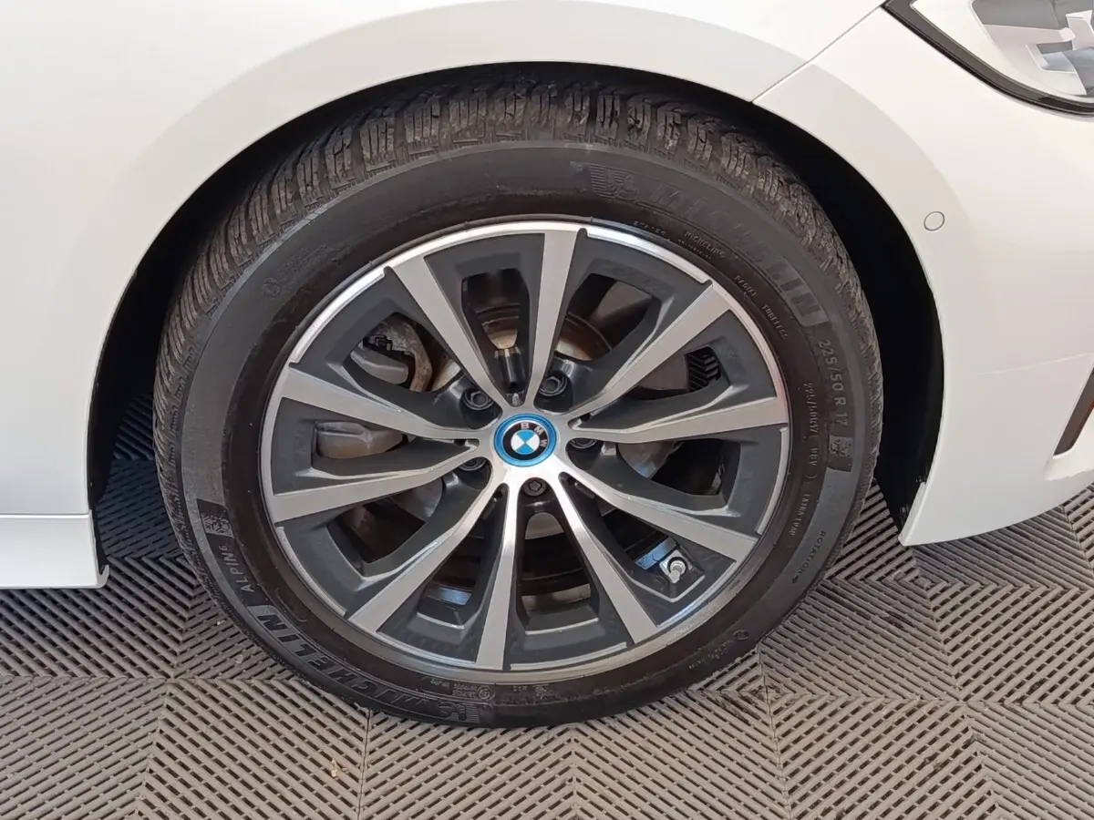 Gros plan sur la roue avant droite d'une BMW Série 3 blanche, mettant en valeur la jante alliage bicolore et le logo central.