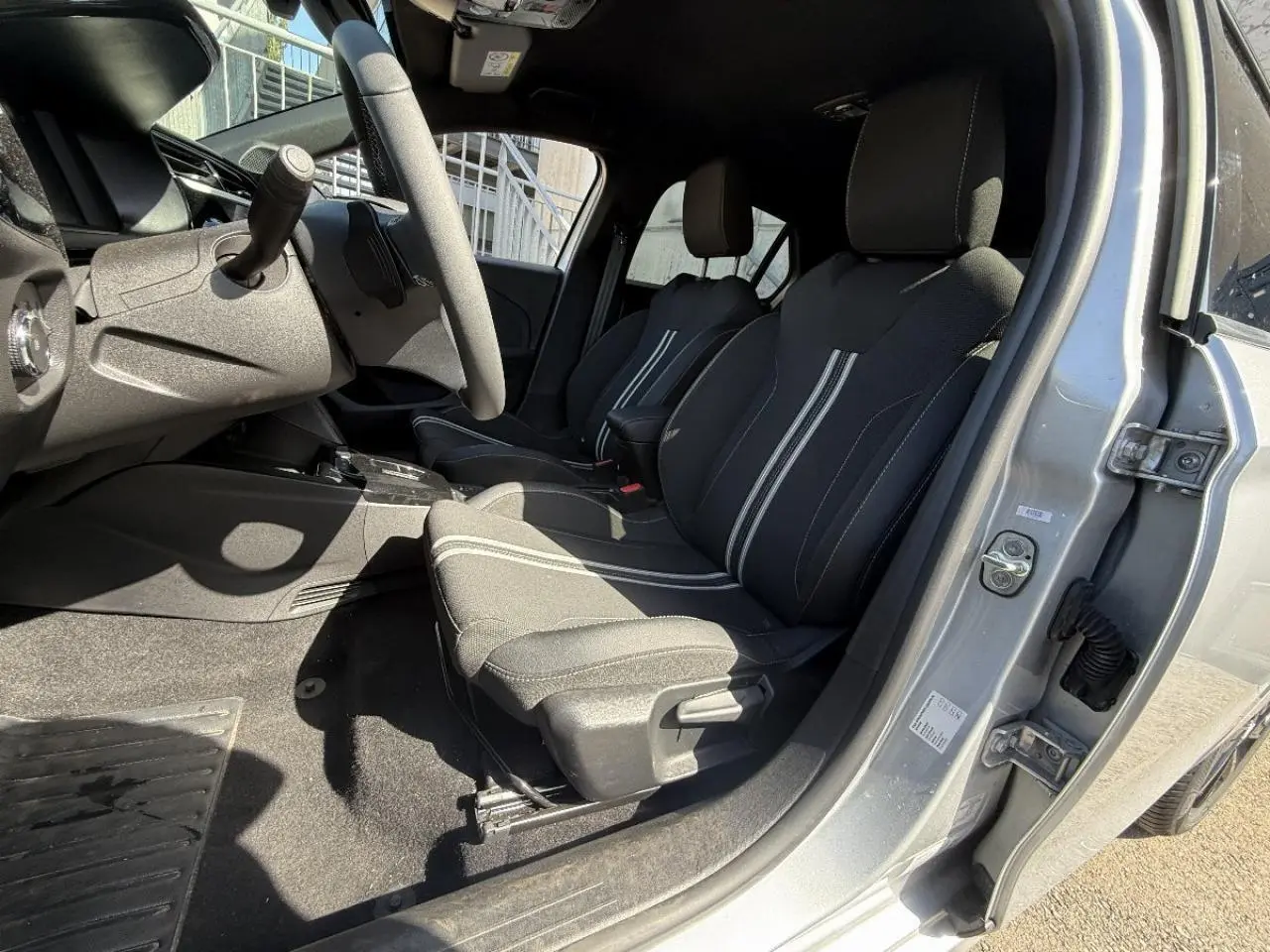 Vue intérieure côté conducteur de l’Opel Corsa 2025 gris aluminium, sièges noirs avec bandes blanches et volant visible.