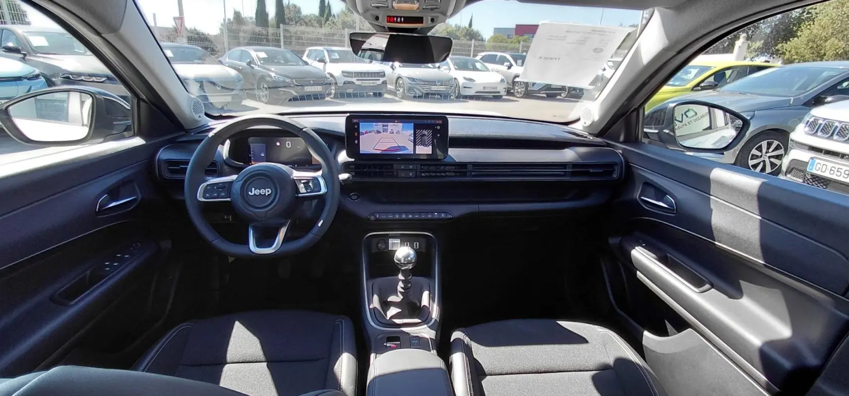 Vue intérieure frontale du Jeep Avenger 2025, tableau de bord noir avec écran tactile et levier de vitesse manuel visible.