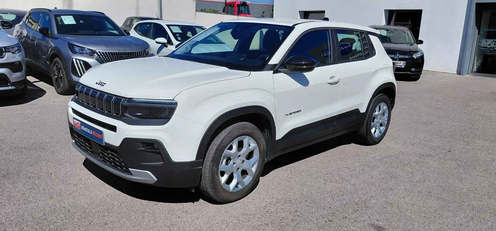 Jeep Avenger blanc en 3/4 avant droit, avec calandre noire distinctive et jantes argentées, stationné en extérieur.